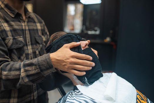 Barber preparing man face for shaving with hot towel on face in barber shop