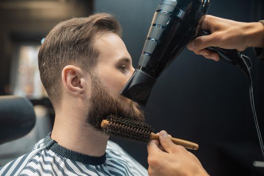 Handsome bearded man is getting hairstyle by hairdresser at the barbershop