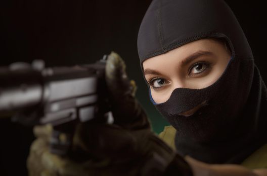 girl in military special clothes posing with a gun in his hands on a dark background in the haze