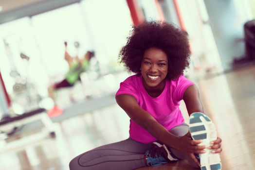 happy young african american woman in a gym stretching and warming up before workout young mab exercising with dumbbells in background