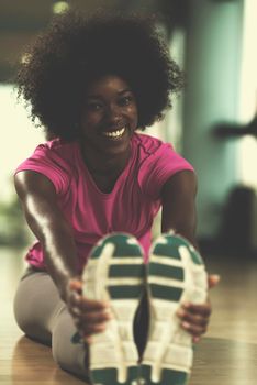 happy young african american woman in a gym stretching and warming up before workout