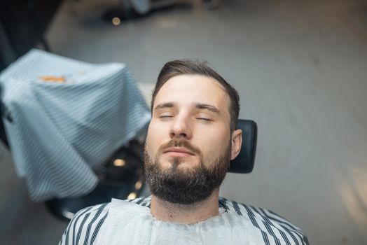 Handsome man with a beard and closed eyes in the barbershop. Closeup.