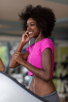 afro american woman running on a treadmill at the gym while listening music on earphones