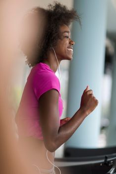 afro american woman running on a treadmill at the gym while listening music on earphones