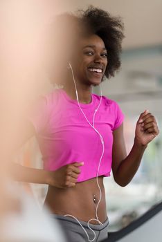 afro american woman running on a treadmill at the gym while listening music on earphones