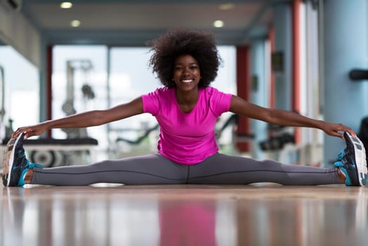 happy young african american woman in a gym stretching and warming up before workout