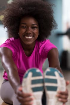 happy young african american woman in a gym stretching and warming up before workout