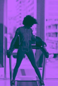 afro american woman running on a treadmill at the gym while listening music on earphones duo tone filter