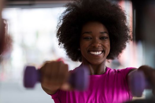 happy healthy african american woman working out in a crossfit gym on weight loss with dumbbells