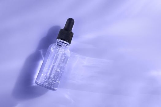 Color of the year 2022. Transparent glass dropper bottle on light violet blue background in the sunlight. Pipette with fluid hyaluronic acid, serum, retinol. Cosmetics, healthcare trendy concept