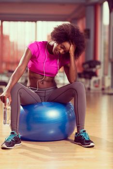 happy african american woman with a curly afro hairstyle in a  gym relaxing after pilates workout