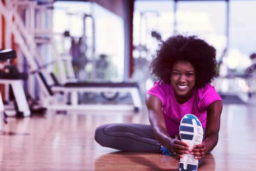 happy young african american woman in a gym stretching and warming up before workout young mab exercising with dumbbells in background