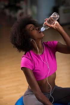 young afro american woman in gym on pilates workout break teaking breath and fresh drinking  water