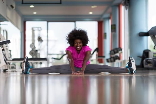 happy young african american woman in a gym stretching and warming up before workout