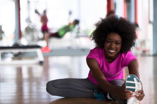 happy young african american woman in a gym stretching and warming up before workout young mab exercising with dumbbells in background