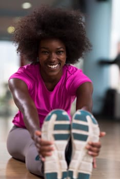 happy young african american woman in a gym stretching and warming up before workout