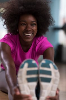 happy young african american woman in a gym stretching and warming up before workout