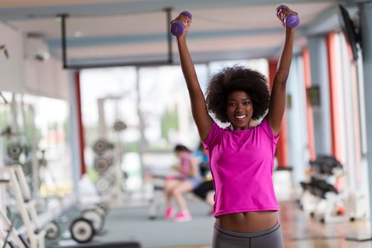 happy healthy african american woman working out in a crossfit gym on weight loss with dumbbells