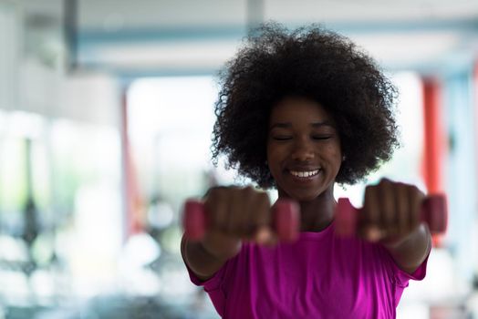 happy healthy african american woman working out in a crossfit gym on weight loss with dumbbells