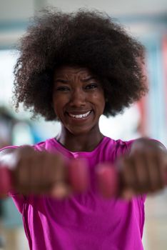 happy healthy african american woman working out in a crossfit gym on weight loss with dumbbells