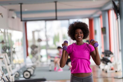 happy healthy african american woman working out in a crossfit gym on weight loss with dumbbells