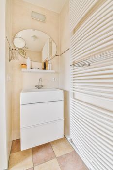 A lovely washbasin with a round mirror with shelves and a radiator near