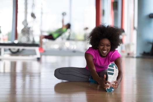 happy young african american woman in a gym stretching and warming up before workout young mab exercising with dumbbells in background