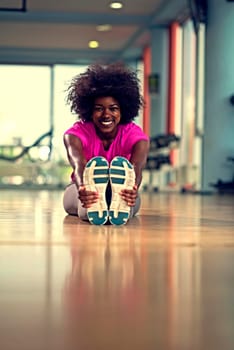 happy young african american woman in a gym stretching and warming up before workout