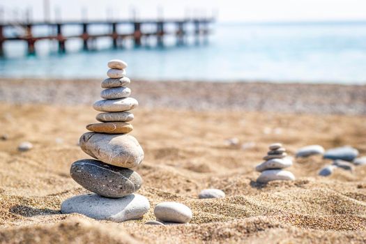 Pyramid of stones for meditation lying on the sand on blurred sea background. The concept of relaxation and rest.