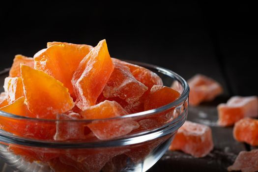 Natural farm homemade candied pumpkin fruits sprinkled with powdered sugar in a glass bowl on a wooden table.