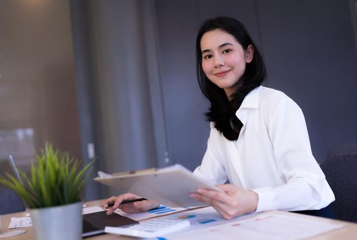 Portrait. Asian Office girl looking at camera and smiling working on company information, Laptop computers, office equipment at the workplace. Banner and copy space.