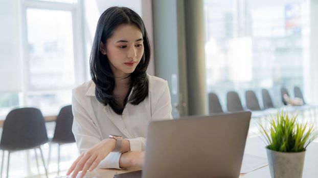 Asian Confident businesswoman in white shirt is working hard on the laptop computer in modern office.