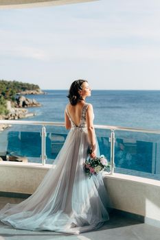 the bride in a beautiful wedding dress stands on the balcony overlooking the sea. High quality photo