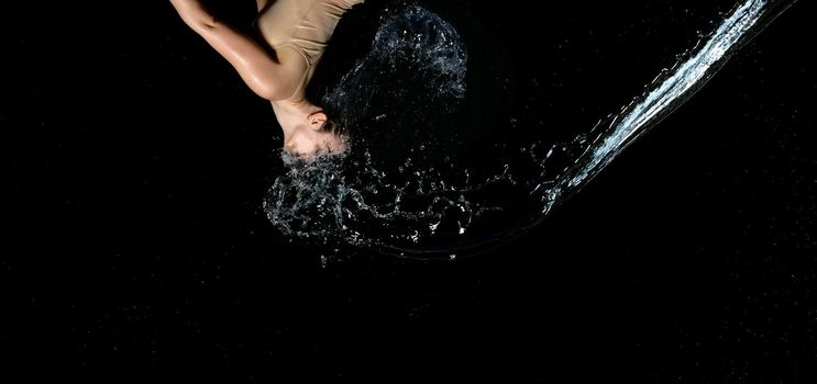 beautiful woman of Caucasian appearance with black hair in drops of water on a black background. A jet of water flies in the face