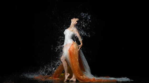 beautiful woman of Caucasian appearance with black hair dances in drops of water on a black background. Woman wearing white corset and skirt, passion pose