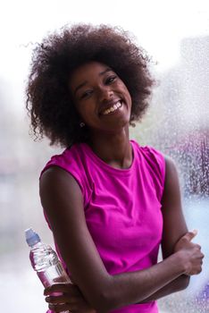 portrait of young afro american woman in gym on work out break while teaking breath and fresh water rainy day and bad weather outdooor