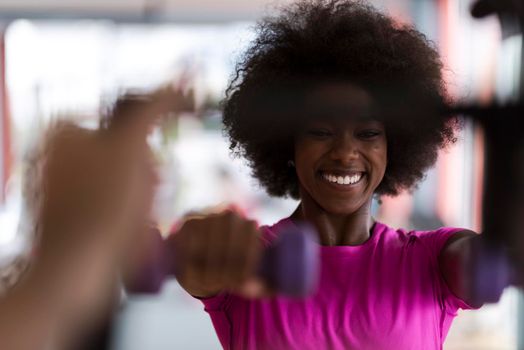 happy healthy african american woman working out in a crossfit gym on weight loss with dumbbells