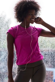 portrait of young afro american woman in gym on workout break while listening music on earphone  and dancing  rainy day and bad weather outdooor