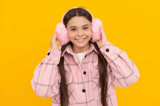 Happy kid smile in warm winter wear and fur ear warmers yellow background, earmuffs.