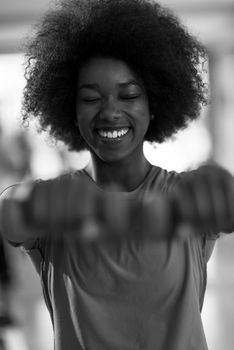 happy healthy african american woman working out in a crossfit gym on weight loss with dumbbells