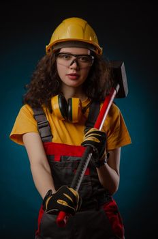 girl in the construction helmet and overalls with a sledgehammer