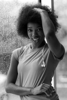 portrait of young afro american woman in gym on workout break while listening music on earphone  and dancing  rainy day and bad weather outdooor