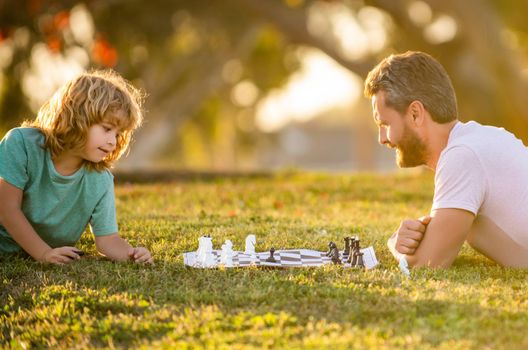 father and son playing chess in morning park. fathers day. happy family. parenthood and childhood. checkmate. spending time together. strategic and tactic. tutorship. dad and kid play logic game.