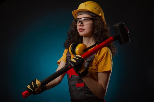 girl in the construction helmet and overalls with a sledgehammer