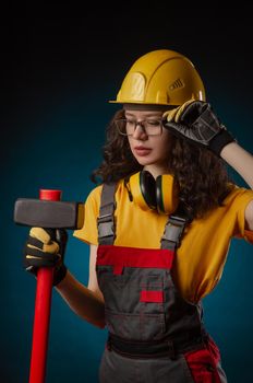 girl in the construction helmet and overalls with a sledgehammer