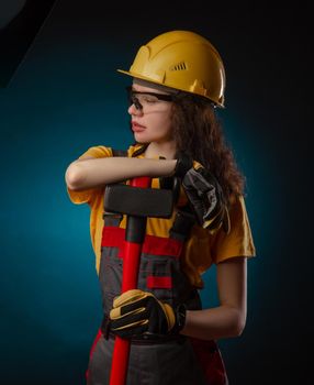 girl in the construction helmet and overalls with a sledgehammer