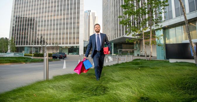 happy successful man in formalwear with shopping bags and present box walk outside the office, mens day.