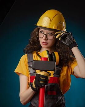 girl in the construction helmet and overalls with a sledgehammer