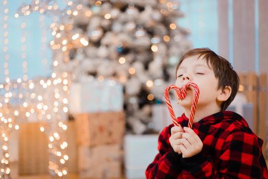 A boy in pajamas with caramel under the Christmas tree . New Year's candies are red. New Year's mood.