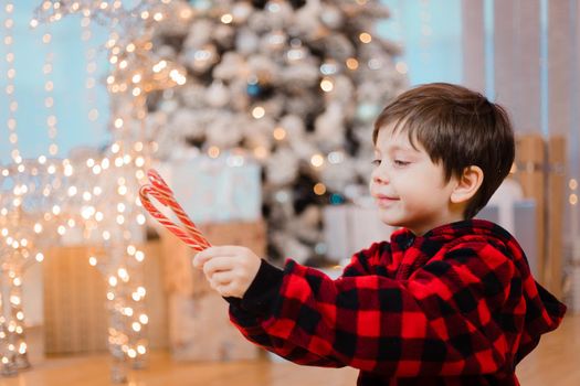 A boy in pajamas with caramel under the Christmas tree . New Year's candies are red. New Year's mood.